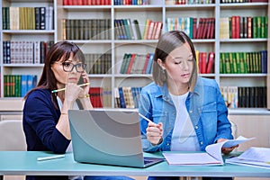 Female university student with teacher preparing for exam, inside library