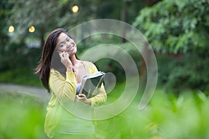 Female university student using her phone, standing in a park.