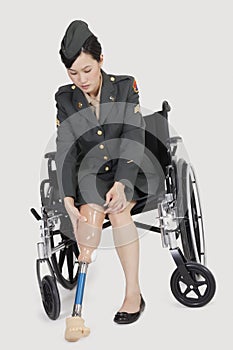 Female US military officer in wheelchair holding artificial limb over gray backgrounds