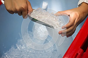 Female use metal ice scoop and plastic cup in ice bucket