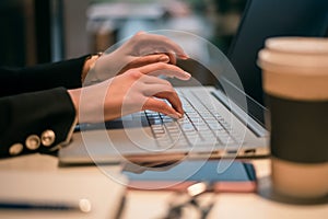 Female using her laptop at a cafe. Side view of young woman sitting at a table with a cup of coffee and mobile phone surfing the