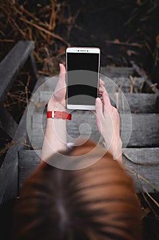 Female using phone with big black screen display, and red sportwatch. Outdoor, dark autumn tones, mobile and internet