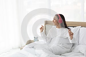 Female using red headphone on bed at home. Young girl wearing pajamas sitting on bed at bedroom  listening to music with headphone