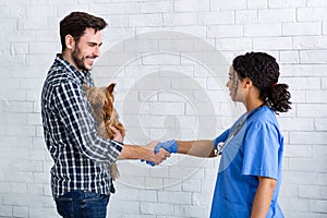 Female vet doc and young owner of little dog shaking hands in animal hospital