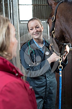 Female Vet Examining Horse In Stables With Owner
