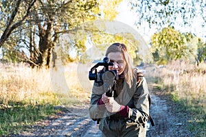 Female videographer holding a gimbal with mirrorless camera. Woman with stabilized camera rig filming outdoors on a sunny