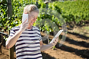 Female vintner using digital tablet while talking on mobile phone