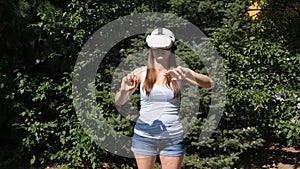 Female in virtual reality glasses controls the device with his hands against the background of green trees