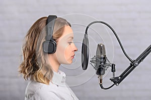 Female vocal recording. Young girl with microphone and headphones in recording studio. Recording of vocal, blogger, reading text,