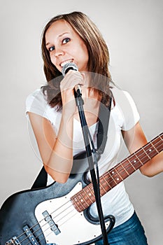 Female vocalist with microphone and bass guitar on gray