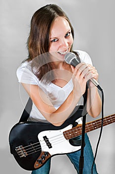Female vocalist with microphone and bass guitar on gray