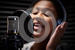 Female Vocalist Wearing Headphones Singing Into Microphone In Recording Studio