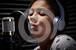 Female Vocalist Wearing Headphones Singing Into Microphone In Recording Studio photo