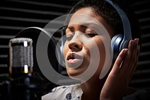 Female Vocalist Wearing Headphones Singing Into Microphone In Recording Studio