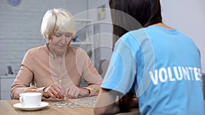 Female volunteer and aged woman collecting puzzles, Alzheimer disease awareness