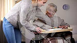 Female volunteer serving dinner to handicapped old woman, elder care, help