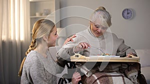 Female volunteer serving dinner to handicapped old women, elderly sitter service