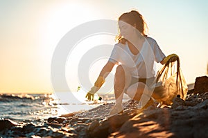 A female volunteer squats and picks up plastic bottles on the ocean shore. Copy space. Cleaning of the coastal zone