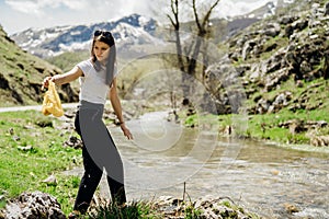 Female volunteer walking along river bank, picking up litter.Cleaning nature from plastic waste.Active responsible woman