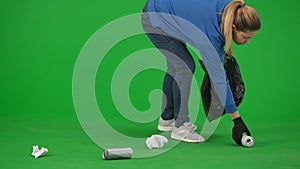 A female volunteer wearing black gloves and carrying a trash bag picks up trash on the green screen. The woman puts