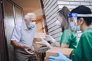 Female volunteers in mask gives an elderly man boxes with food near his house. Quarantined, . Coronavirus covid-19. photo