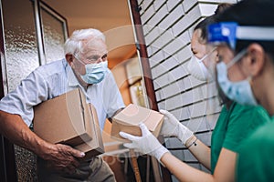 Female volunteers in mask gives an elderly man boxes with food near his house. Quarantined, . Coronavirus covid-19. photo