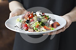 The female waiter holding in her hands plate with greek salad