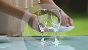 Female waiter putting plates and glasses on table, outdoor restaurant, catering
