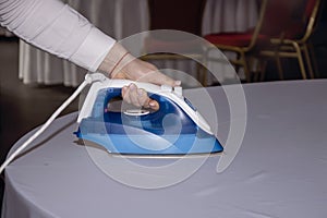 A female waiter in a restaurant irons a tablecloth with an iron in a dark room