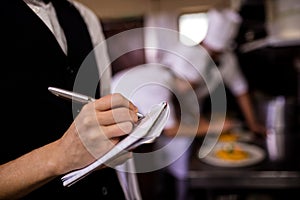 Female waitress noting an order on notepad in kitchen