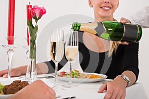 Female Waitress Pouring Champagne Into Glass For Couple