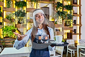 Female waitress wearing face shield, visor serves the coffee in restaurant during coronavirus pandemic representing new normal