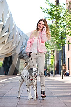 Female walking her dog outdoors and talking on mobile phone
