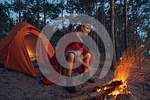 Female warming up near campfire while wearing blanket on shoulders