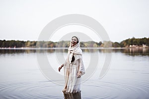 Female wearing a biblical robe and laughing while standing in the water