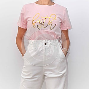 Female wearing a pink t-shirt with the word faith on it with white high-waisted jeans