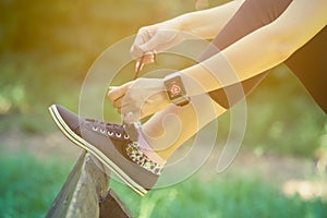 Female wearing smart watch and tying shoelaces in the park