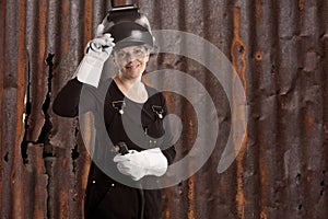 Female welder standing in front of a old rusty metal wall