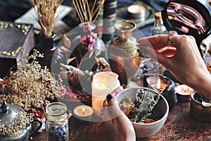 Female wiccan witch holding grey clay pot in her hands preparing ingredients for a spell at her altar photo