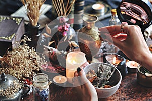 Female wiccan witch holding grey clay pot in her hands preparing ingredients for a spell at her altar