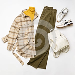 Female winter or autumn stylish clothing set. Plaid checkered shirt, yellow sweater, green corduroy trousers, sneakers and