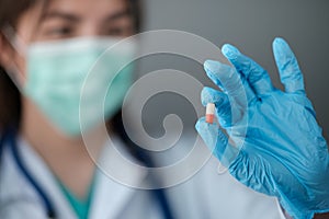 Female woman doctor holding up a pill vitamin supplement drug cure on grey background