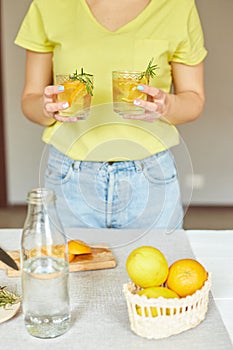 Female woman hand hold two glasses of citrus orange and rosemary fresh lemonade
