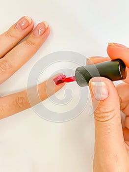 Female woman painting her nails in red color on a white background
