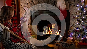 Female in woolen knitted socks drinking hot chocolate at fireplace 4K Christmas