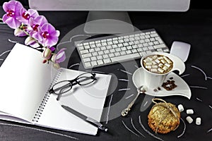 Female work space with computer, orchid, coffee and notebook with glasses and pen on black background.