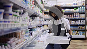 Female worker arranging products on shelves in milk department in supermarket, slow motion