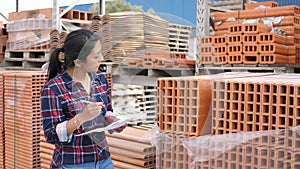 Female worker checking quantity of red bricks in warehouse of building materials