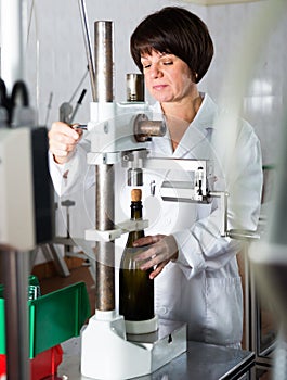 Female worker corking wine bottles with machine