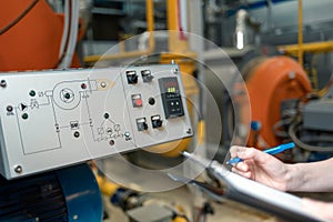 A female worker with a folder and a pen in her hand, writing meter readings. In the background-boiler room. Industrial production